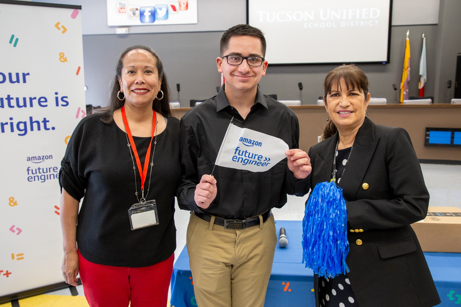 Ƶapp High senior Anthony Talavera smiles and poses with an Amazon Future Engineer flag and two TUSD staff members