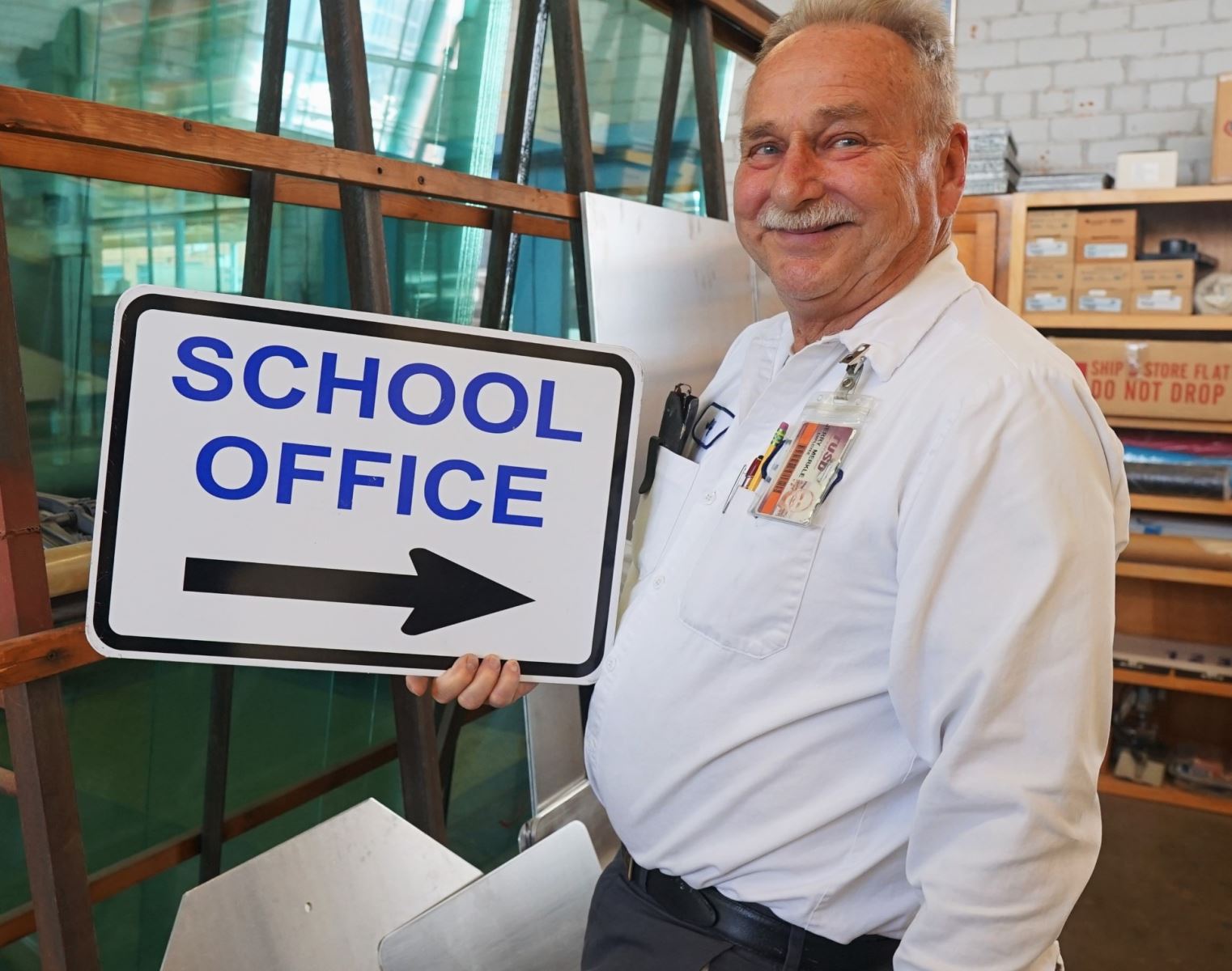 Jerry Merkle smiles with his sign reading School Office